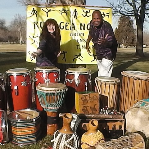 Woman and man standing behind a variety of drums.