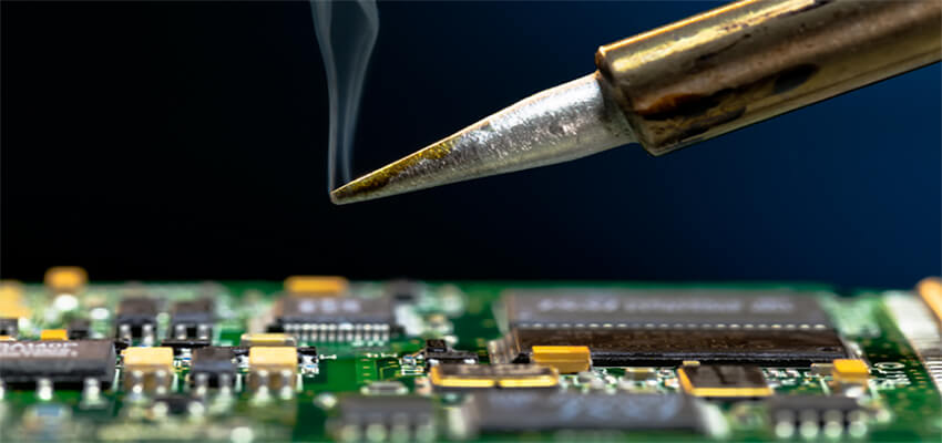 Image of the tip of a soldering tool hovering over a circuit board. A wisp of steam is coming from the soldering tool.