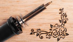 Image of woodburning tool lying on a board which has a flower design burned into it