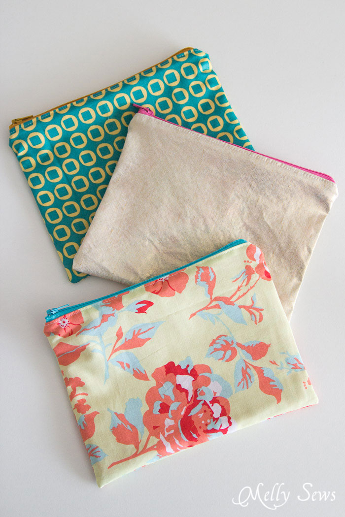 Image of three rectangular zippered fabric pouches. One is pink, one has a blue and yellow geometric pattern, and one has a pink and blue floral pattern.