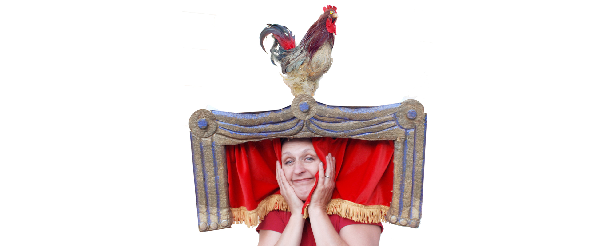 Woman wearing a hat that looks like a stage complete with red curtain and a rooster sitting on top of the stage