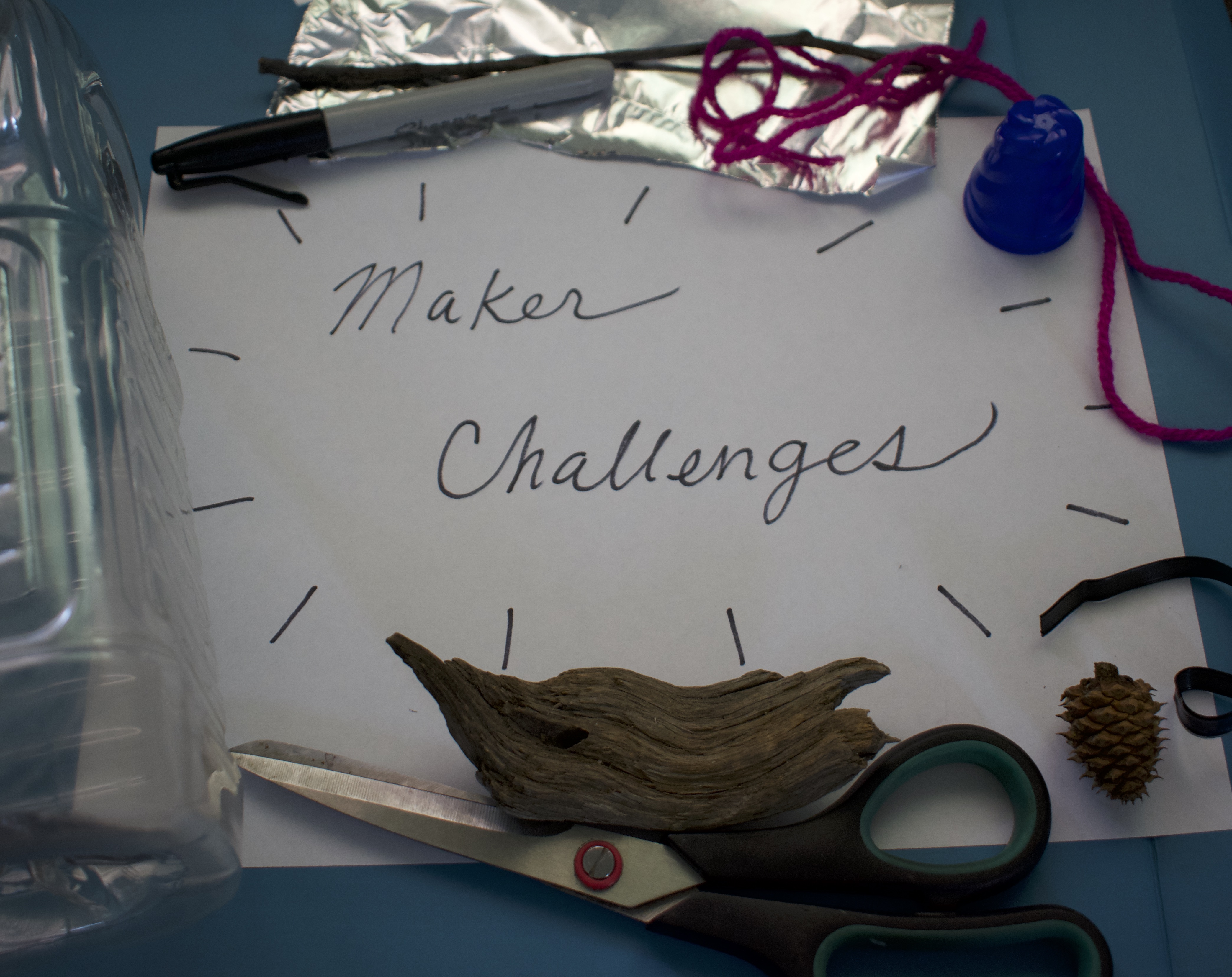 Assorted crafting materials laid out as a frame around piece of paper with the text "Maker Challenges"