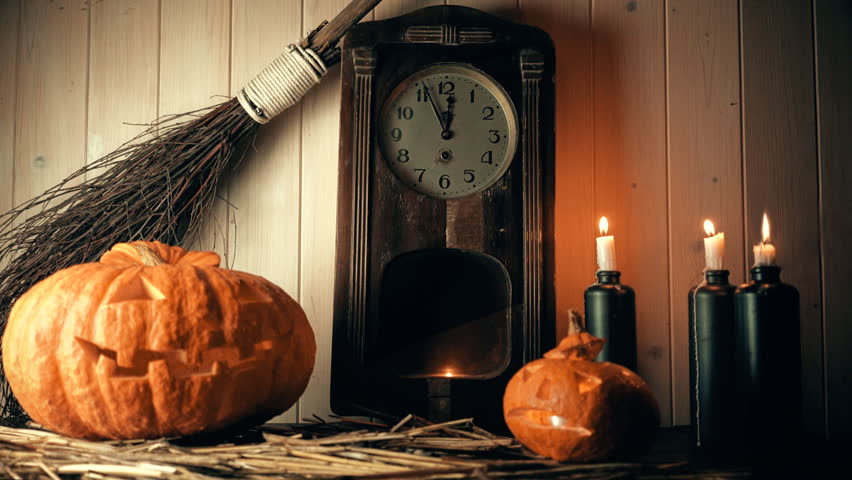 Carved pumpkins on table with little clock and broomstick behind it. There are three unlit candles to the right and one small pumpkin in the very front. 
