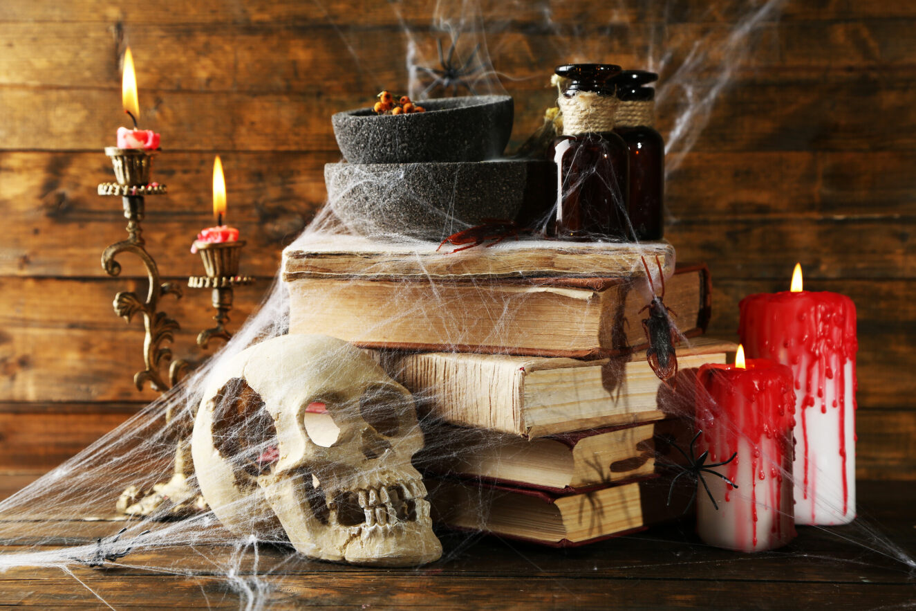 Spooky image of a skull, webs, candles, and books. 