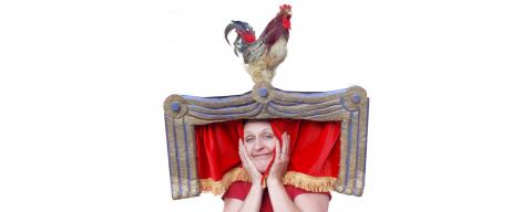 Women wearing hat that look like a stage complete with red curtain and rooster sitting on top of stage