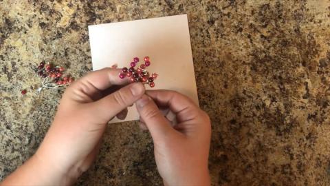 Close up of hands stringing beads on a wire.