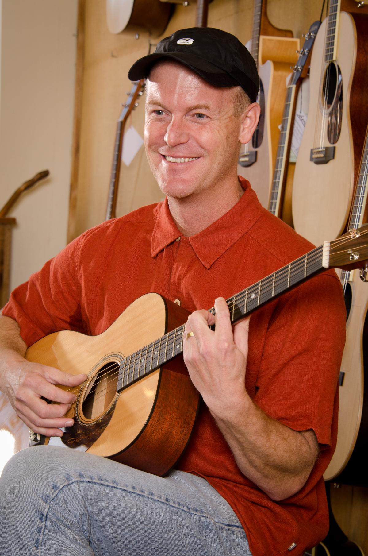 Man in baseball cap playing guitar.